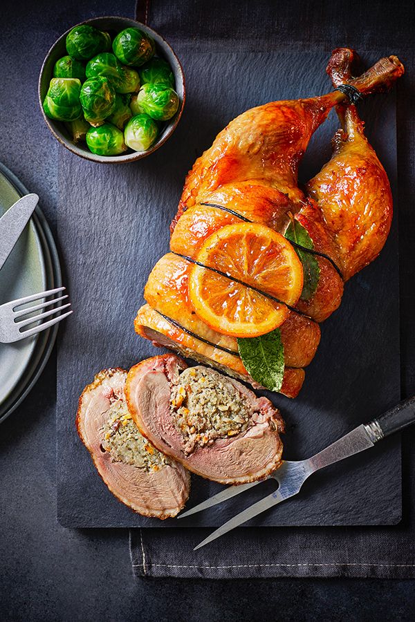 Roasted stuffed turkey with citrus garnish on a slate board, served with Brussels sprouts on the side.