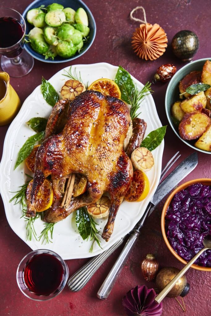 Roasted duck with citrus and herbs on a festive dinner table with side dishes and wine.