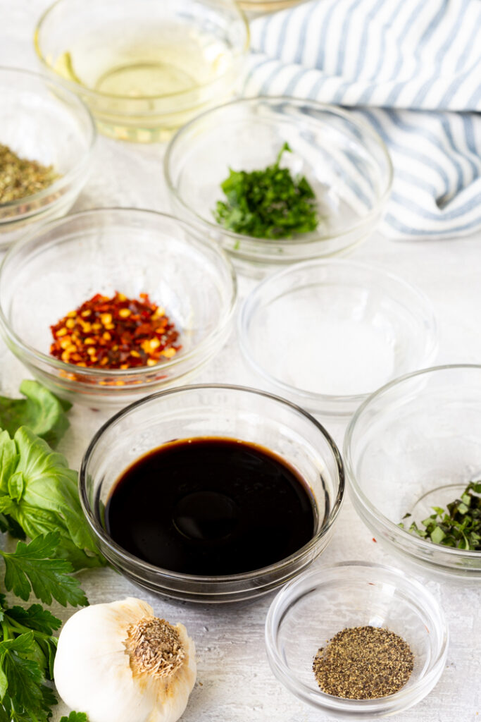 Bowls of herbs, spices, oil, and soy sauce on a table with garlic and basil, ready for cooking preparation.