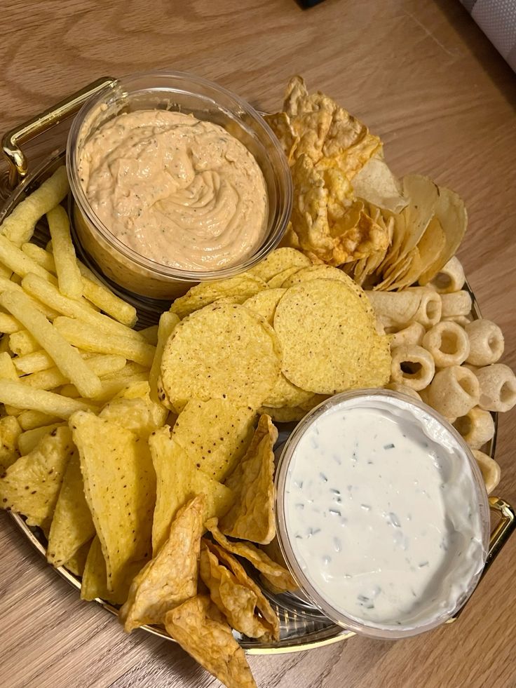 Snack platter with chips and dip varieties including cheese nachos, potato chips, and creamy dips on a wooden table.