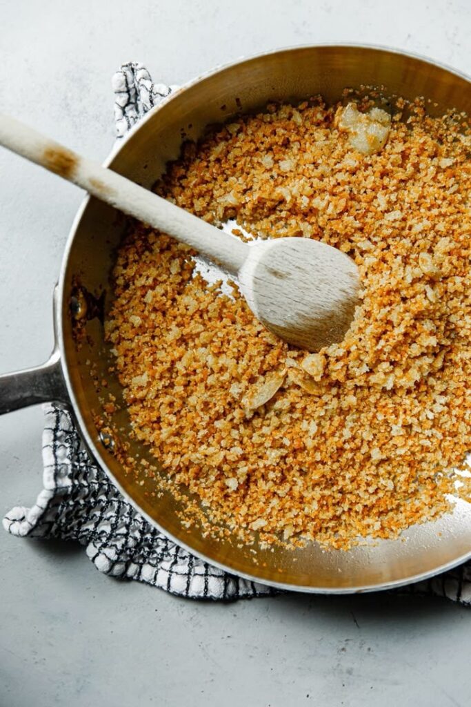 Golden toasted breadcrumbs in a skillet with a wooden spoon on a checkered cloth, perfect for topping recipes.