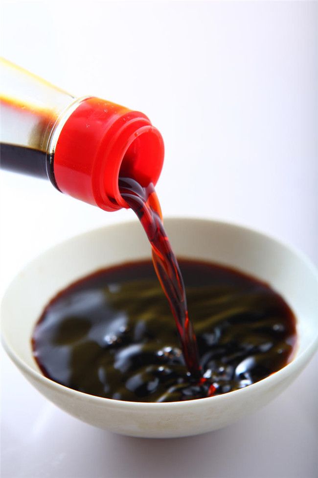 Pouring soy sauce into a white bowl, enhancing flavor in Asian cuisine dishes.