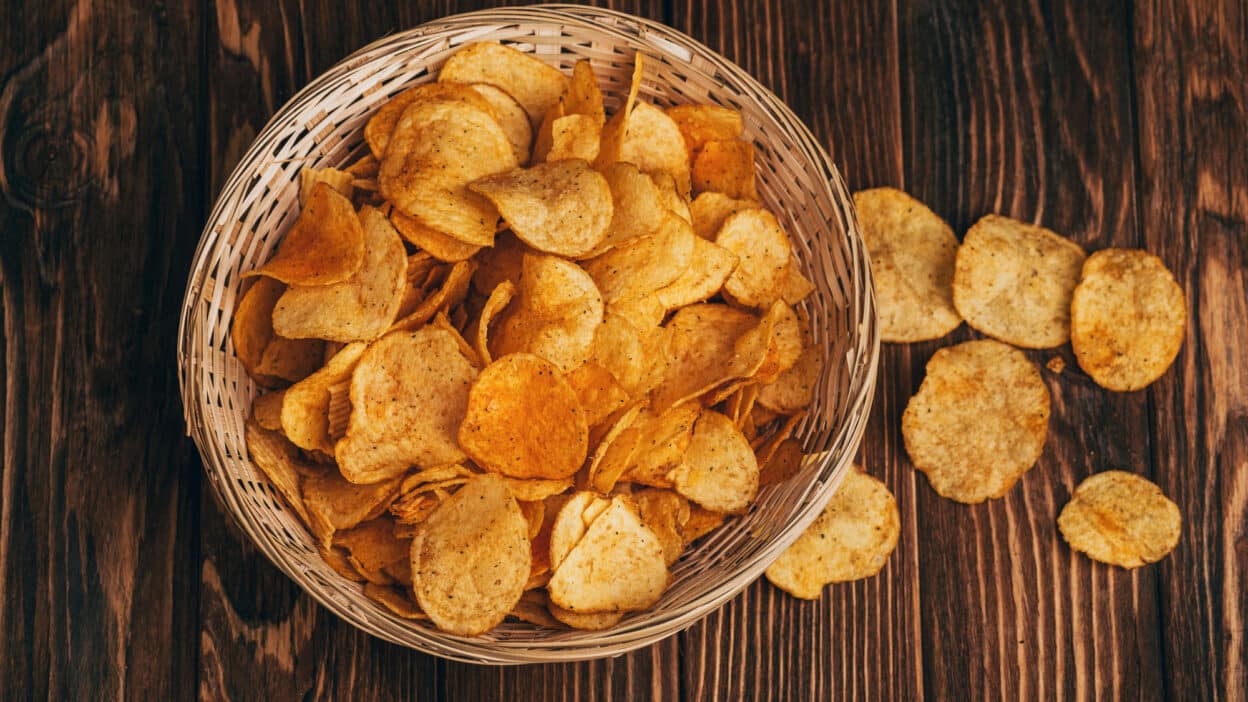 Basket of crispy potato chips on a rustic wooden table, perfect for snack ideas or sharing with friends.