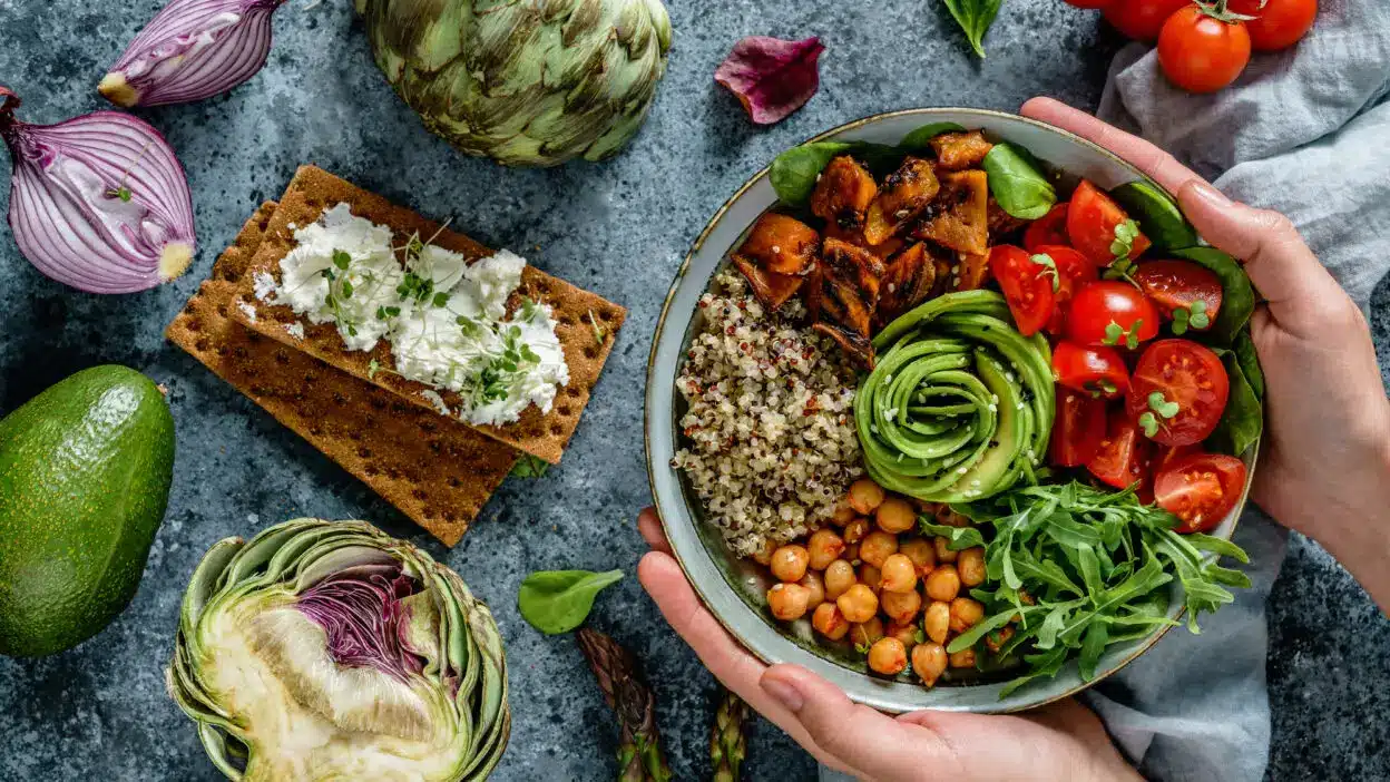 Healthy vegan Buddha bowl with quinoa, chickpeas, avocado, and tomatoes. Fresh ingredients surround the dish.