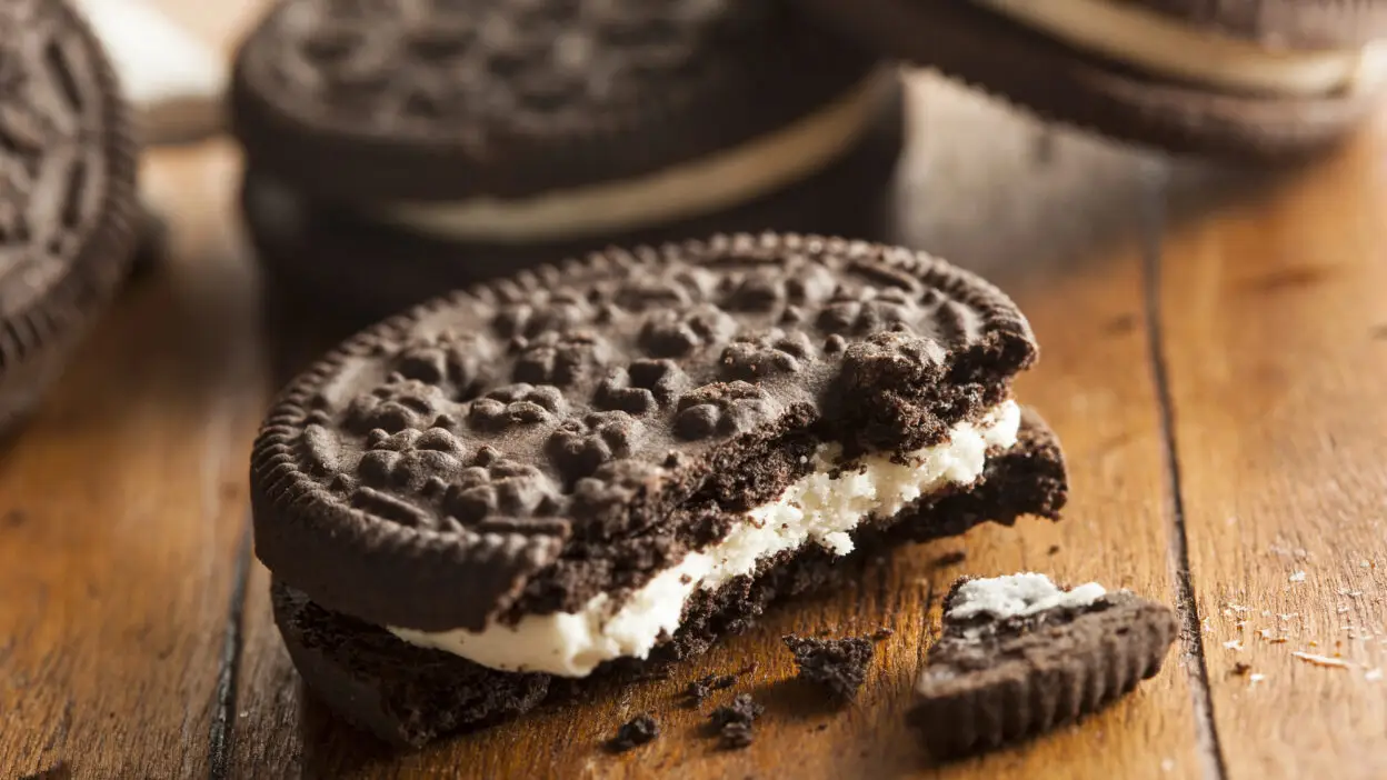 Close-up of a chocolate sandwich cookie with cream filling, half bitten, on a wooden table.