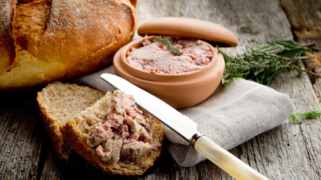 Rustic bread with pâté and herbs on a wooden table, highlighting a creamy spread and inviting presentation.