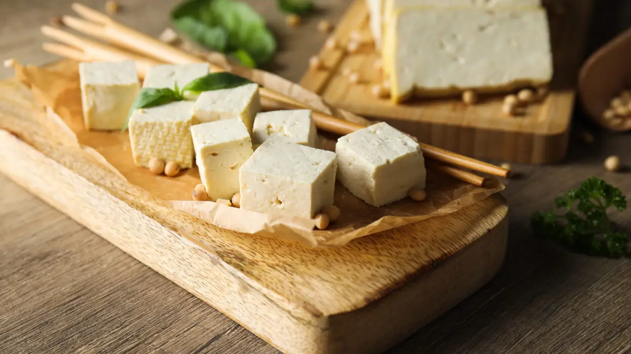 Cubes of fresh tofu on a wooden board with chopsticks and herbs, perfect for plant-based meals and healthy recipes.