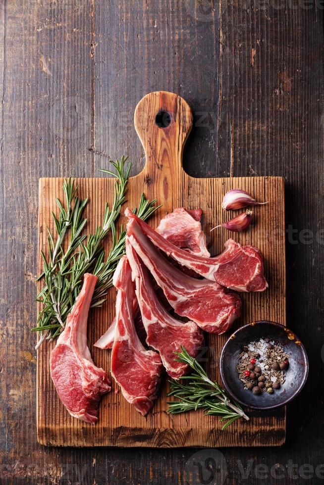 Raw lamb chops with rosemary on a wooden board with garlic and spices. Rustic food preparation concept.