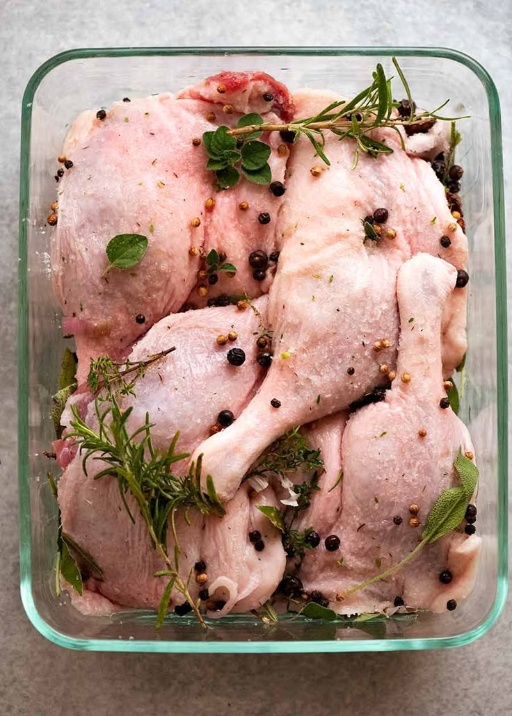 Raw chicken with herbs and spices in a glass dish, ready for marinating and cooking.