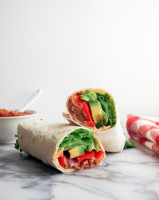 Vegetable wrap with avocado, red peppers, and lettuce on marble surface; side of salsa visible in background.