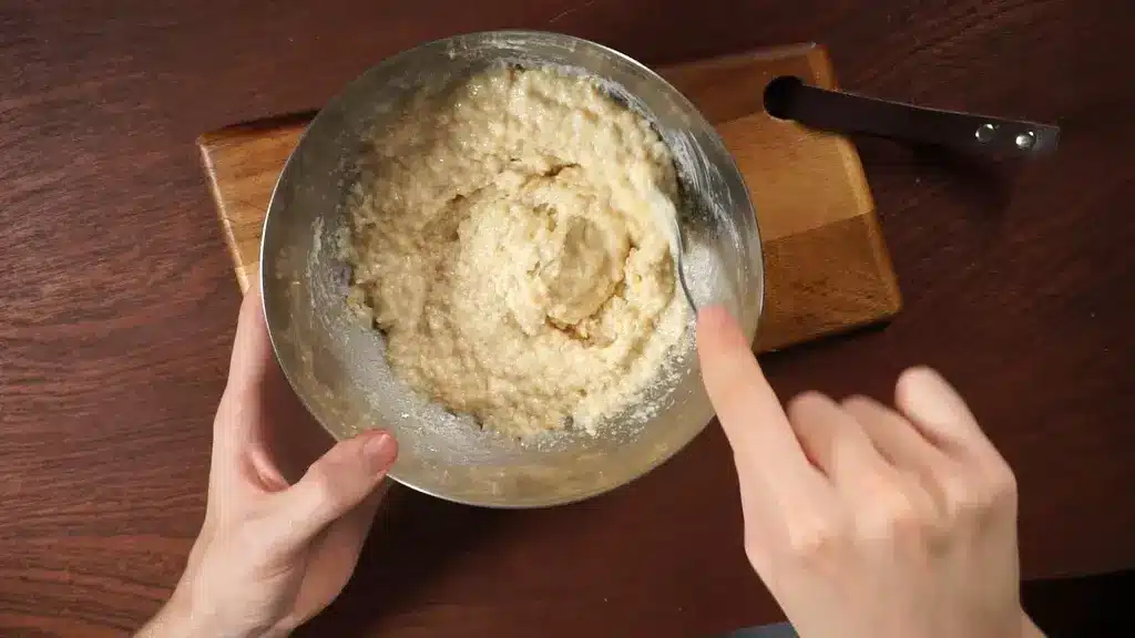Mixing cake batter in a metal bowl on a wooden cutting board with a spoon.