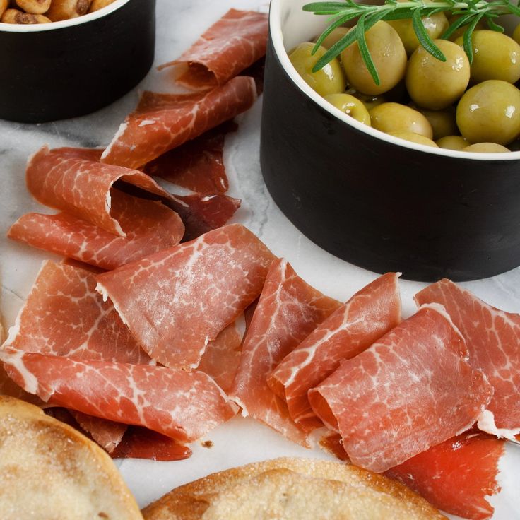 Sliced prosciutto with olives and toasted bread on a marble plate, perfect for appetizers or charcuterie boards.