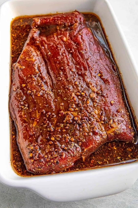 Marinated beef brisket in flavorful sauce, ready for baking in a white dish. Perfect for a savory dinner.