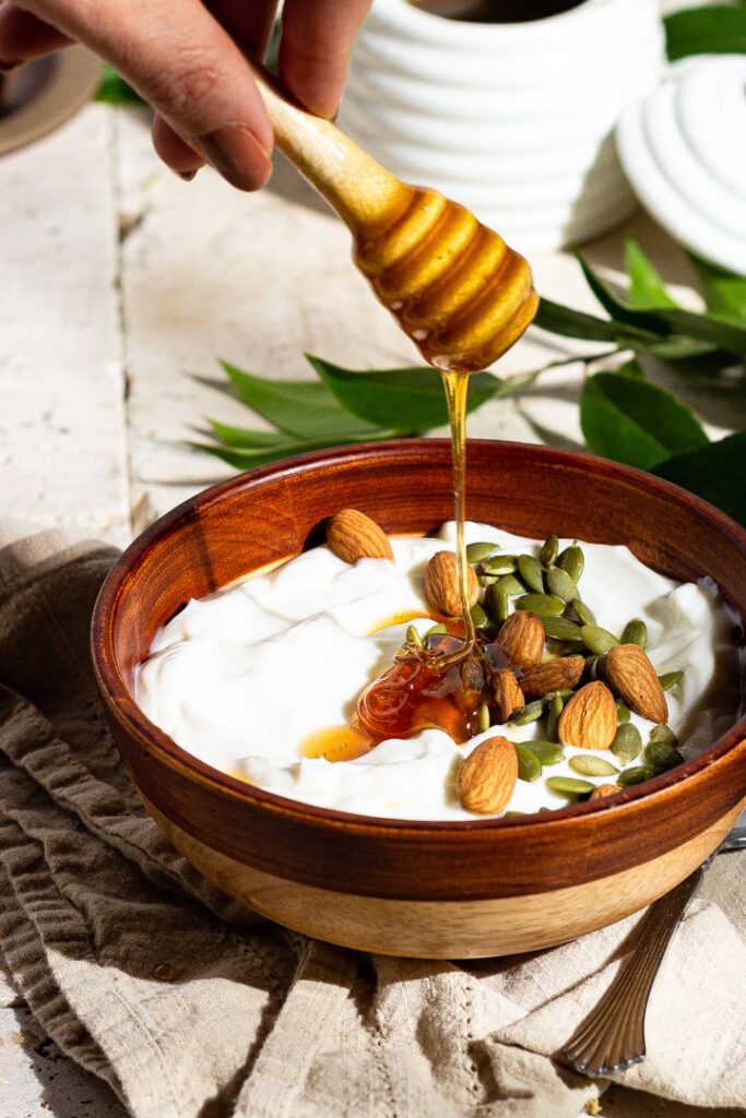 Bowl of yogurt topped with almonds, seeds, and honey drizzle, showcasing a healthy breakfast option.