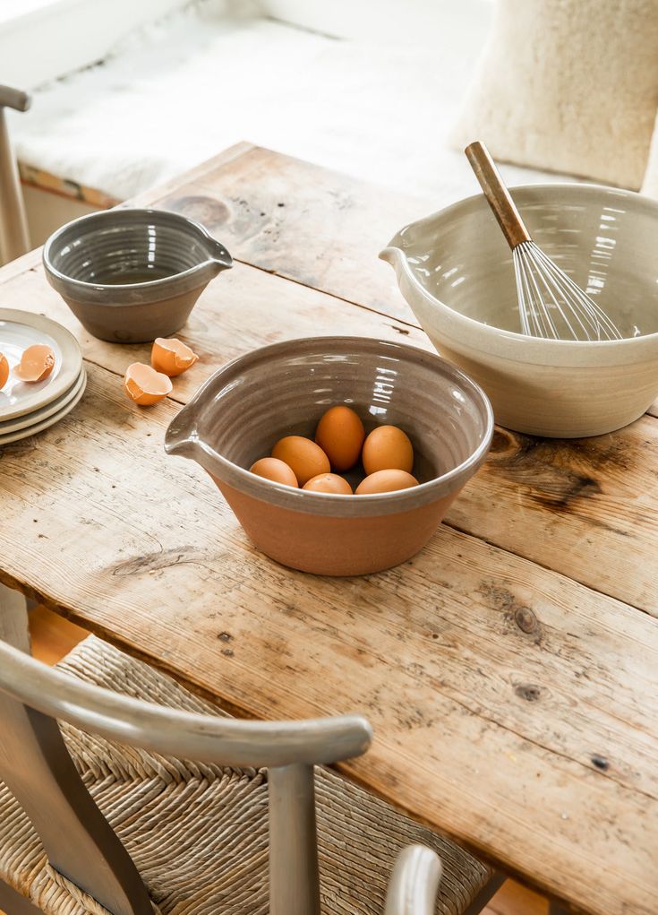 Rustic kitchen scene with mixing bowls, eggs, and a whisk on a wooden table. Perfect for cooking and baking inspiration.