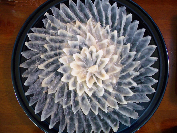 Beautifully arranged sashimi slices on a black plate, resembling a delicate flower pattern for elegant presentation.