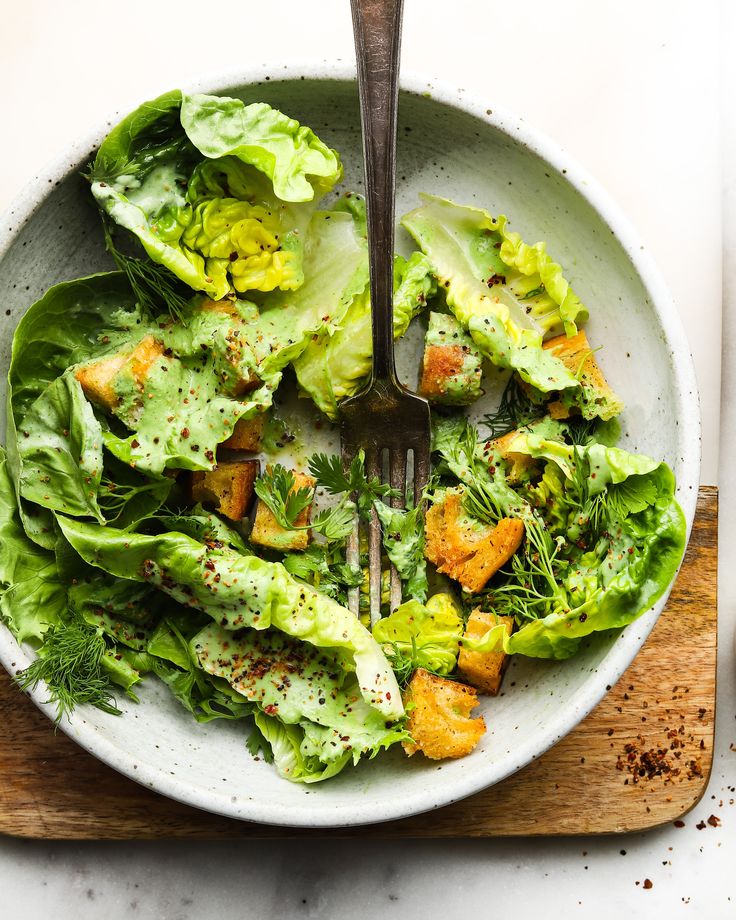 Fresh green salad with croutons and creamy dressing in a bowl on a wooden board, topped with herbs and spices.