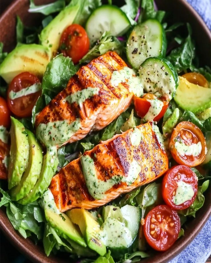 Grilled salmon salad with avocado, cherry tomatoes, cucumbers, and greens, topped with a creamy herb dressing.
