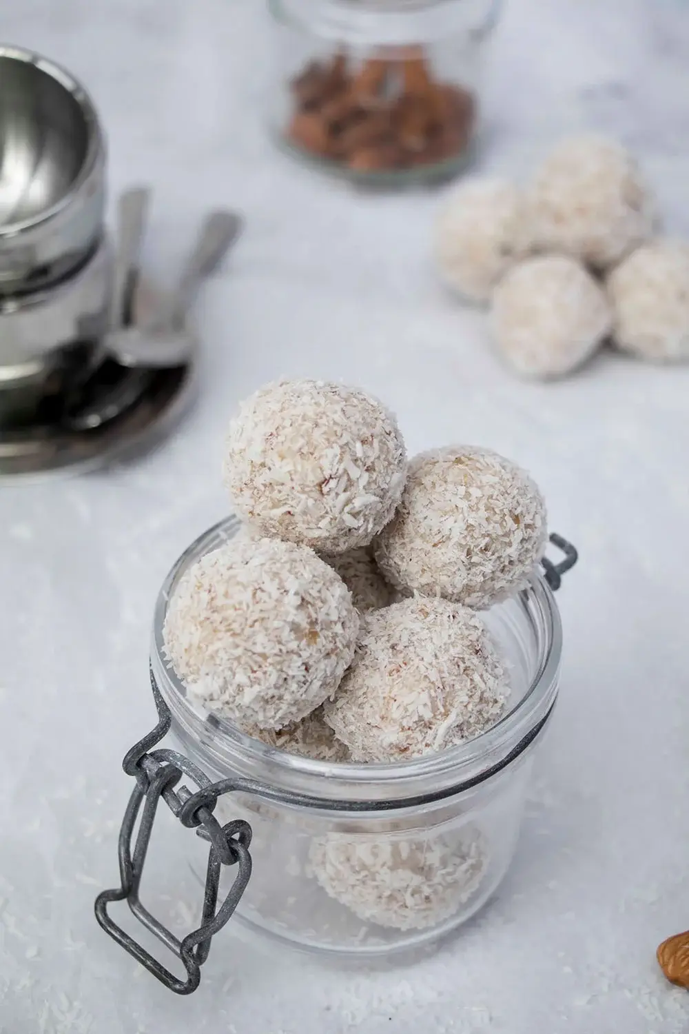 Coconut-covered energy balls in a glass jar on a light background, perfect for healthy snacking or dessert.