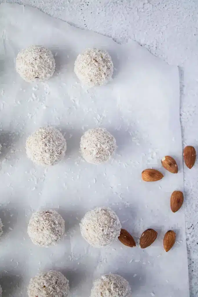 Coconut-covered dessert balls with almonds on parchment paper, perfect for a sweet, nutty treat.