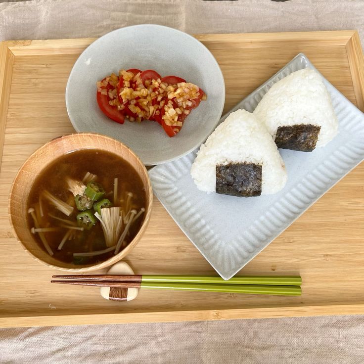 Japanese breakfast tray with onigiri, tomato salad, and miso soup on a wooden background.