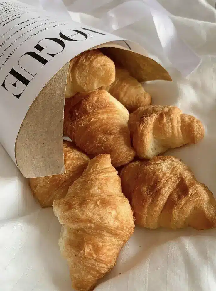Fresh croissants spilling from a paper bag onto a white cloth, perfect for a stylish breakfast display.