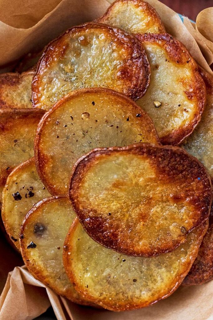 Golden brown roasted potato slices with pepper seasoning on parchment paper. Perfect crispy homemade snack.