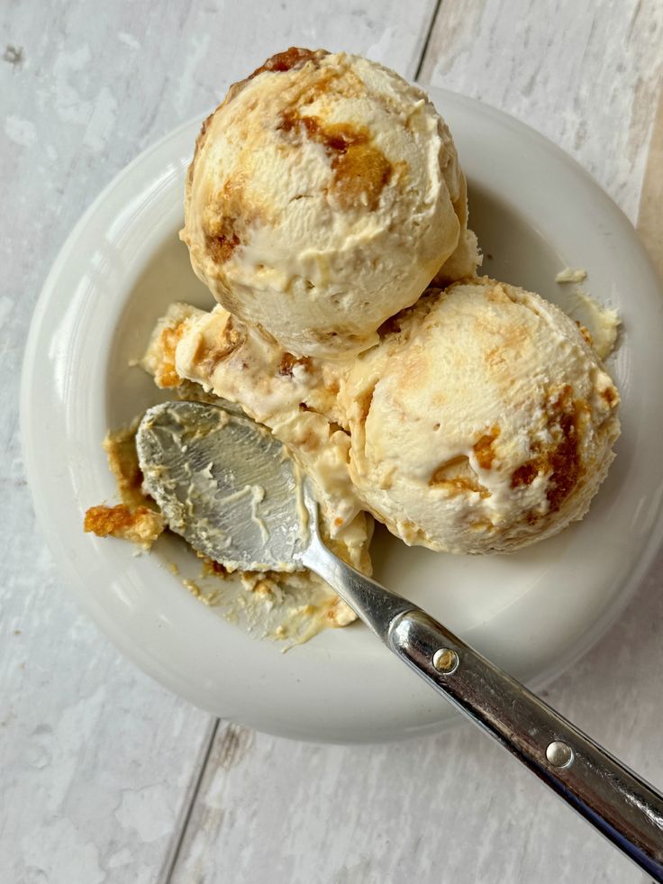 Creamy caramel ice cream scoops on a plate with a metal spoon, inviting dessert lovers on a wooden table background.