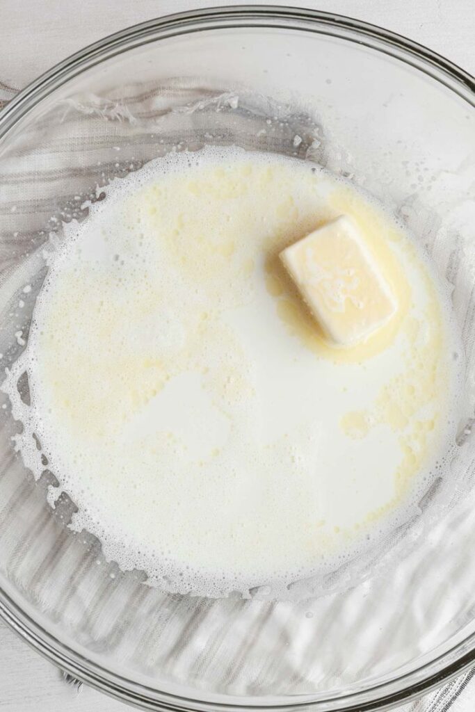 Milk with a stick of butter melting in a clear glass bowl for baking preparation.