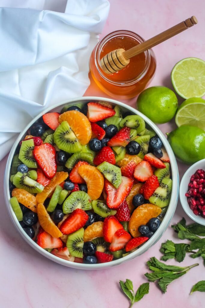 Fresh fruit salad with strawberries, kiwi, blueberries, and oranges, served with honey and limes on the side.
