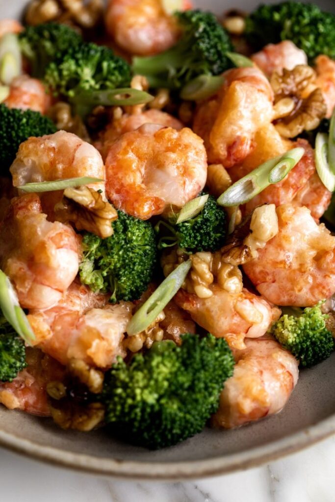 Delicious shrimp stir-fry with broccoli, walnuts, and green onions served in a bowl. Perfect for a healthy meal.