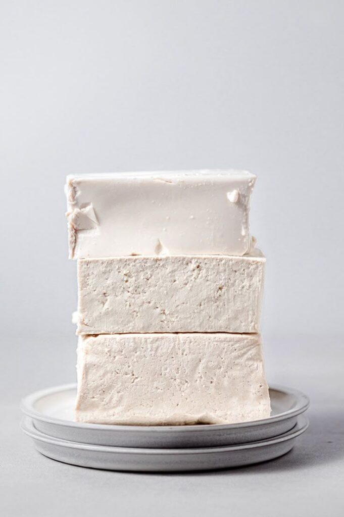 Three stacked homemade marshmallows on a plate, highlighting their fluffy texture against a neutral background.