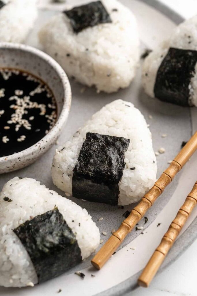 Japanese onigiri with nori served with soy sauce and chopsticks on a white plate.