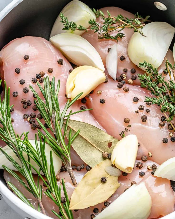 Raw chicken with garlic, onion, bay leaves, rosemary, and peppercorns in a pan, ready for cooking.