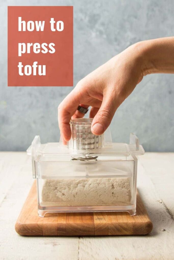 Hand pressing tofu using a tofu press on a wooden board with how to press tofu text overlay.