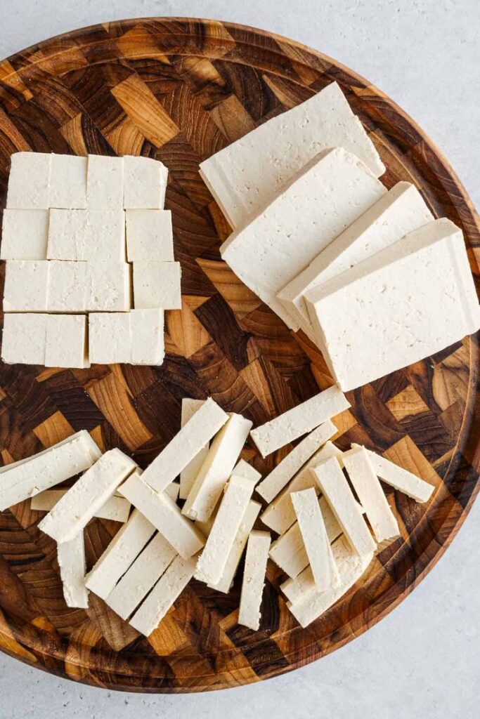 Assorted cuts of tofu displayed on a wooden board.