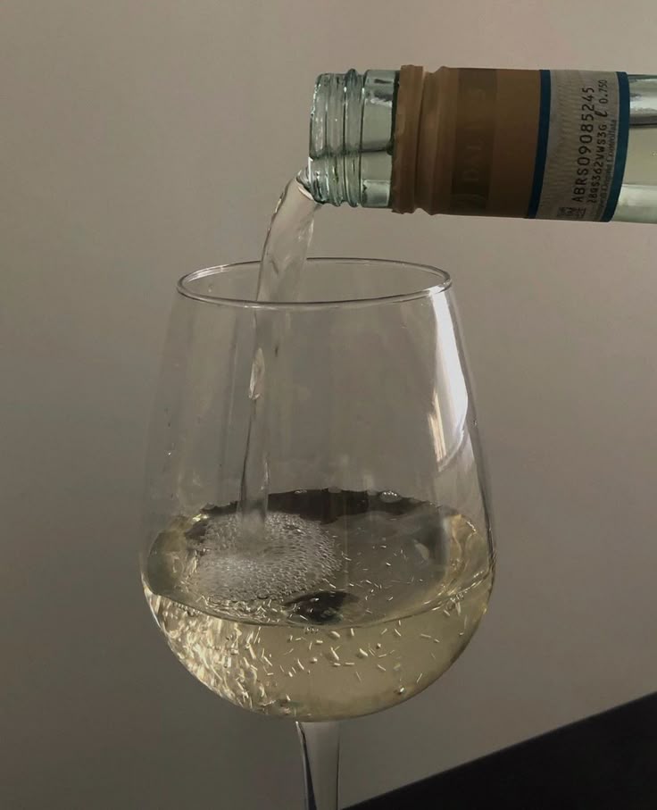 Pouring white wine into a clear glass against a neutral background.