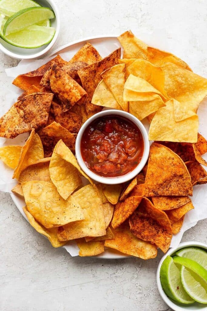 Plate of tortilla chips with salsa in a bowl, surrounded by lime wedges. Perfect for snacking or parties.