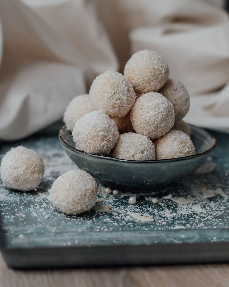 Coconut-covered dessert balls in a bowl on a textured surface, perfect treat for sweet lovers.