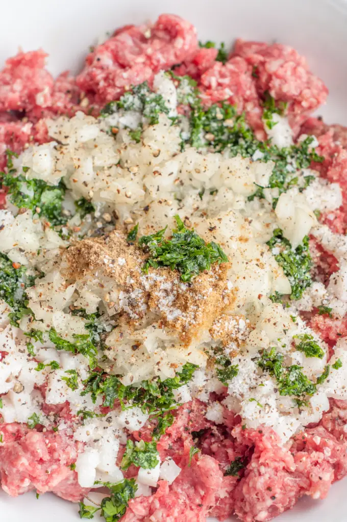 Ground beef mixed with chopped onions, fresh parsley, and spices, ready for cooking.