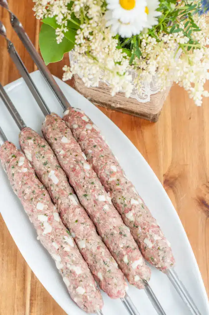 Raw kebabs on skewers with overhead view, flowers in the background, on wooden table. Perfect for grilling recipes.