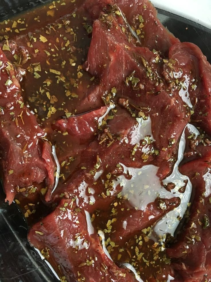 Raw marinated beef slices with herbs and spices in a marinade sauce, ready for cooking or grilling.