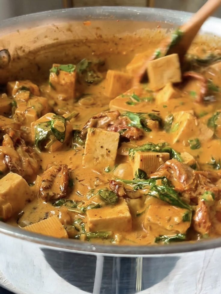 Creamy tofu curry with spinach and spices cooking in a pan. Rich, flavorful vegetarian meal preparation.