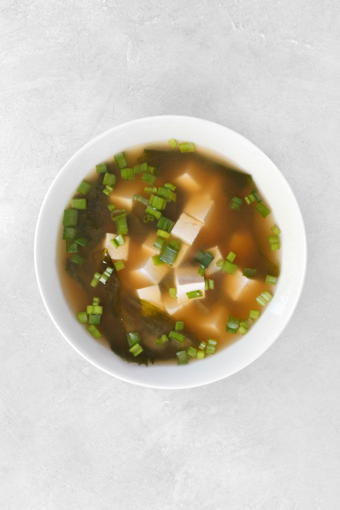 Bowl of miso soup with tofu, seaweed, and green onions on a light background. Perfect for a healthy meal.