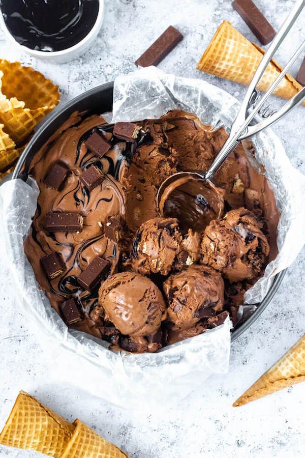 Delicious homemade chocolate ice cream with chunks and sauce, served with waffle cones and scooped in a pan.