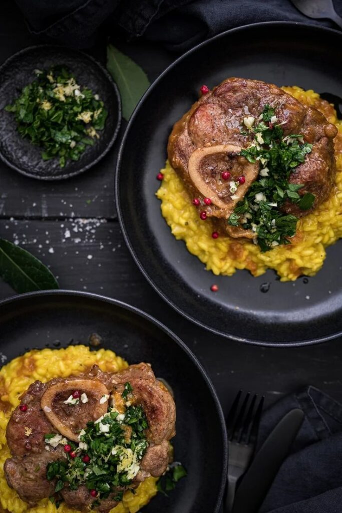 Osso Buco on saffron risotto garnished with gremolata, served on elegant black plates.