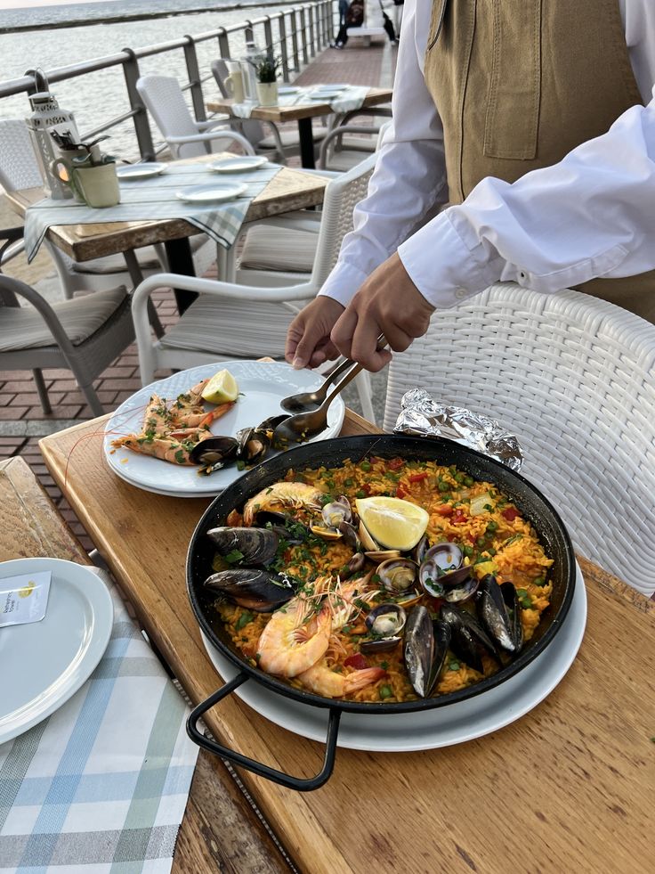 Seafood paella served seaside at a restaurant, garnished with lemon, shrimp, and mussels, waiter serving.
