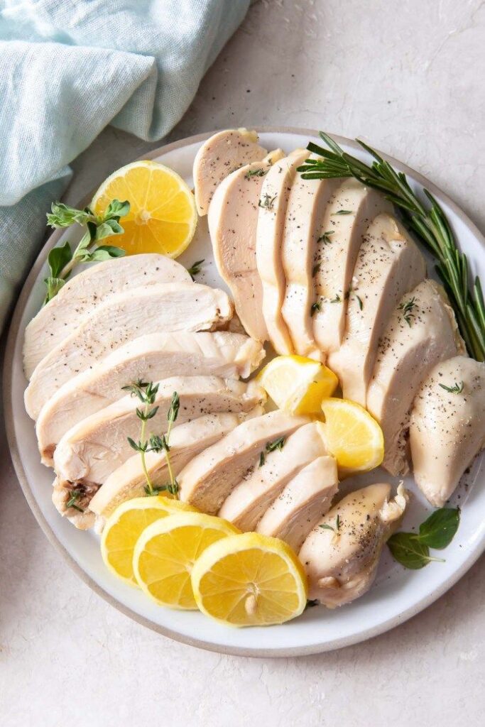 Sliced chicken breast with lemon and herbs on a white plate. Perfect for a healthy meal.