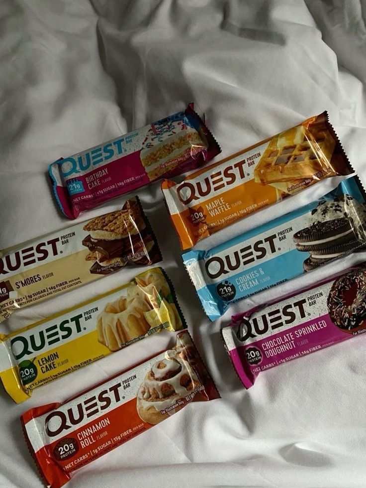 Assorted Quest protein bars on a white surface, featuring flavors like Birthday Cake, S'mores, and Lemon Cake.