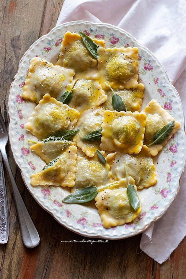 Homemade ravioli on a floral plate, garnished with fresh sage leaves and drizzled with butter sauce.